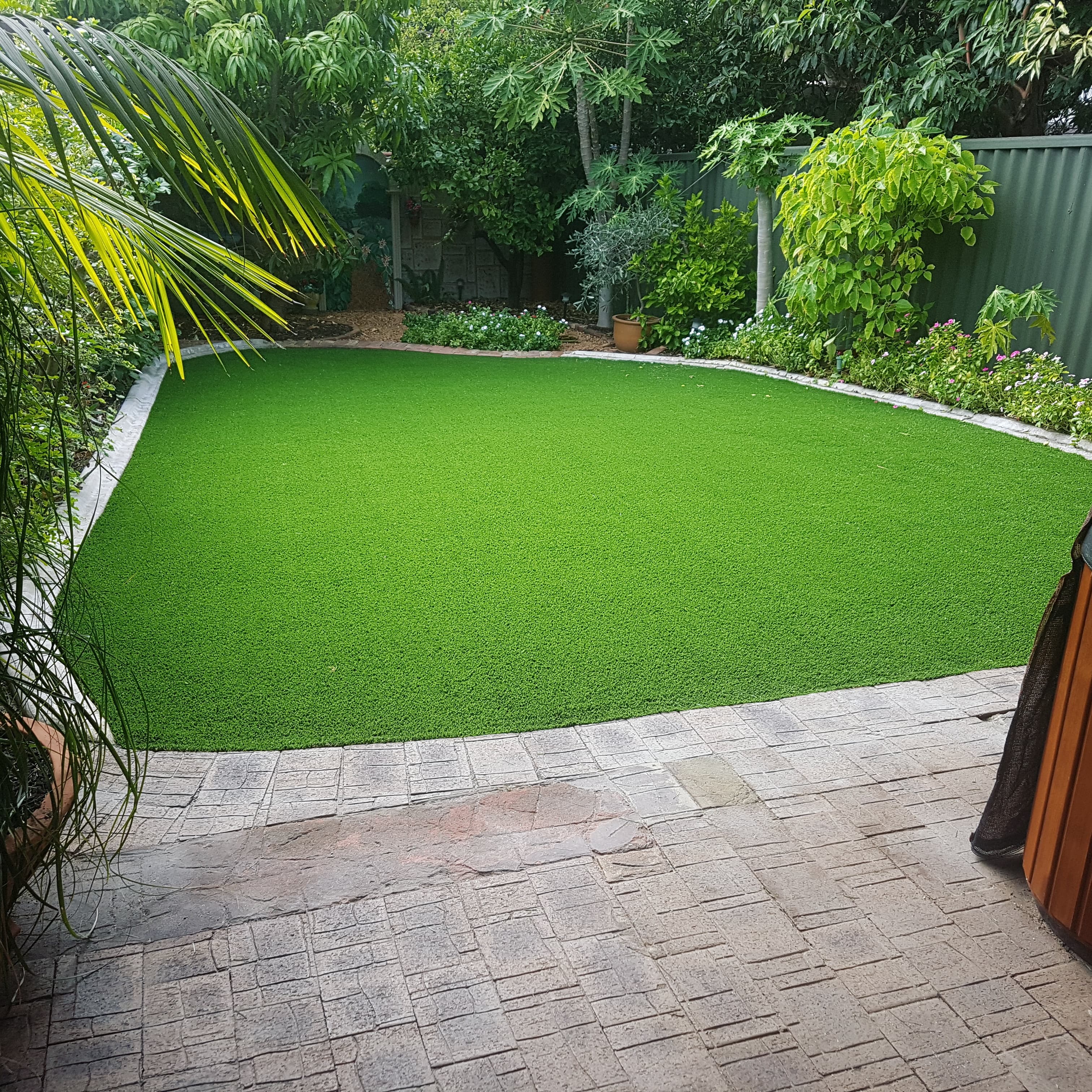 Lush artificial turf backyard surrounded by established gardens, installed by Metro Style Group in Perth